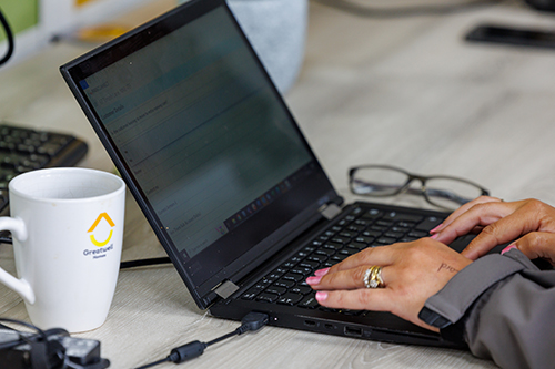 Someone typing on a laptop at a desk. On the desk is a mug with the Greatwell Homes logo on, and a pair of glasses.